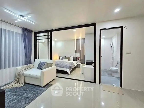 Modern open-plan bedroom with cozy seating area and sleek bathroom access.