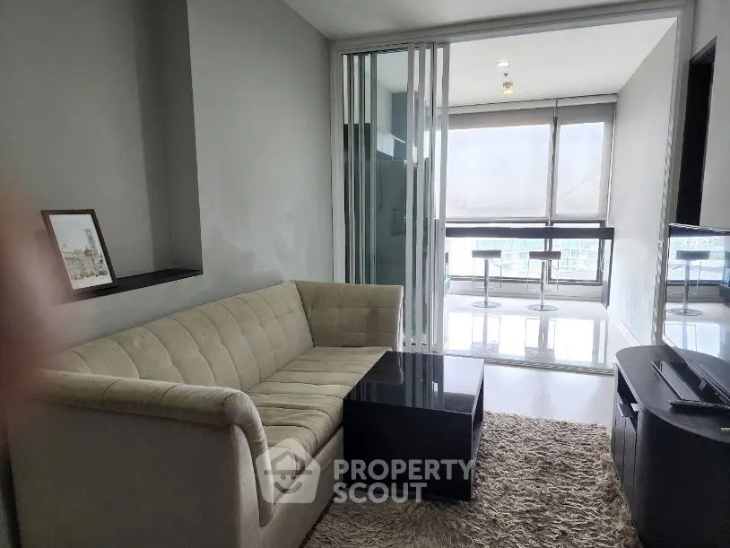 Modern living room with cozy sofa and glass doors leading to a bright balcony with city view.
