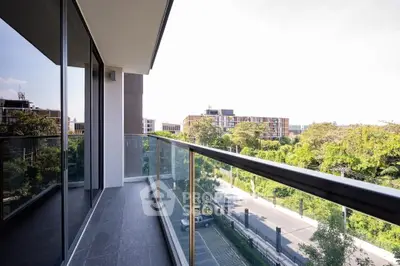 Spacious balcony with glass railing offering a scenic view of lush greenery and modern architecture.