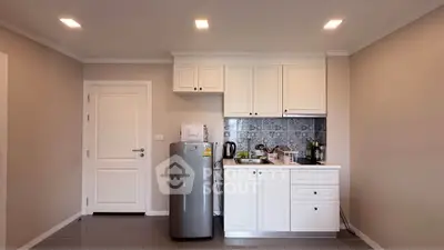 Modern compact kitchen with white cabinets and stainless steel fridge in cozy apartment.