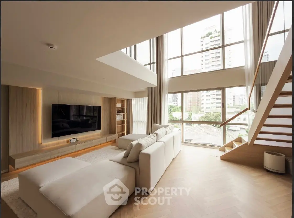 Luxurious living room with high ceilings, large windows, and modern staircase in a stylish apartment.