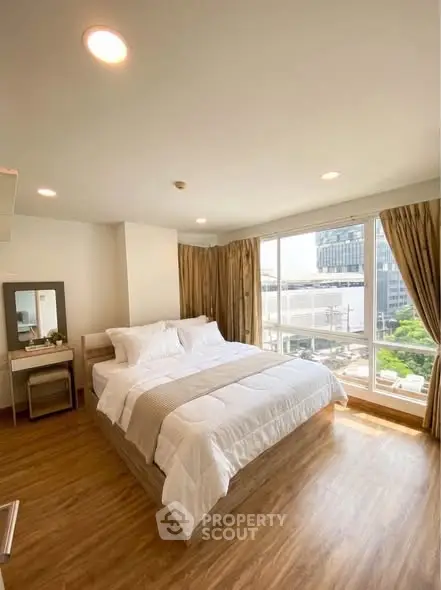 Spacious bedroom with large windows offering a stunning city view, featuring elegant wooden flooring and modern decor.
