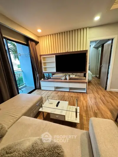 Modern living room with stylish decor and large TV, featuring cozy seating and wooden flooring.