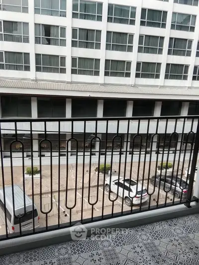 Spacious balcony with modern railing overlooking urban parking area and building facade.