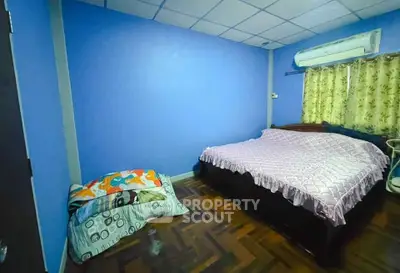 Cozy bedroom with blue walls and parquet flooring, featuring an air conditioner and comfortable bedding.