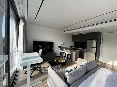 Modern living room with sleek kitchen and large windows offering natural light.