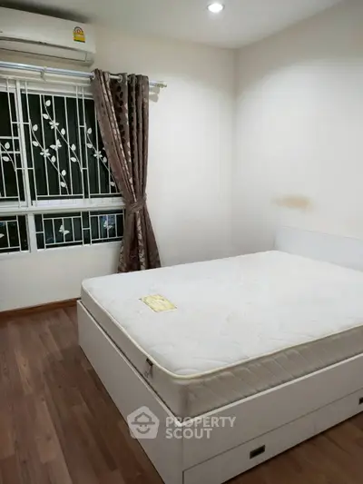 Cozy bedroom with hardwood floors, large window, and air conditioning unit.