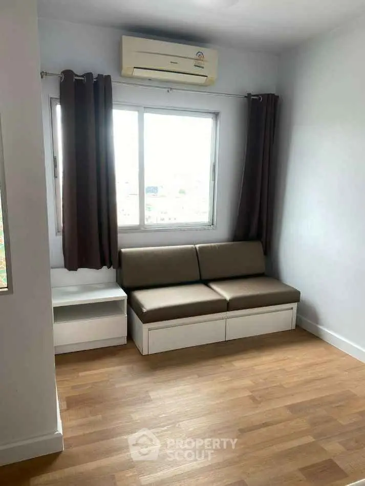 Cozy living room with modern sofa and air conditioning, featuring wooden flooring and natural light.