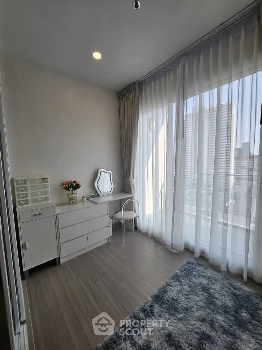 Bright bedroom with modern furniture and large windows offering city views, perfect for urban living.
