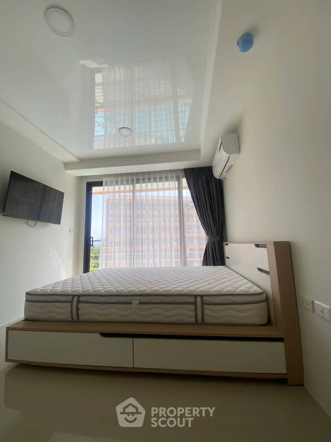 Modern bedroom with sleek design, featuring a large window and wall-mounted TV, perfect for urban living.