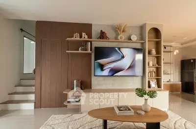 Modern living room with stylish decor and built-in shelving, featuring a large TV and elegant furnishings.