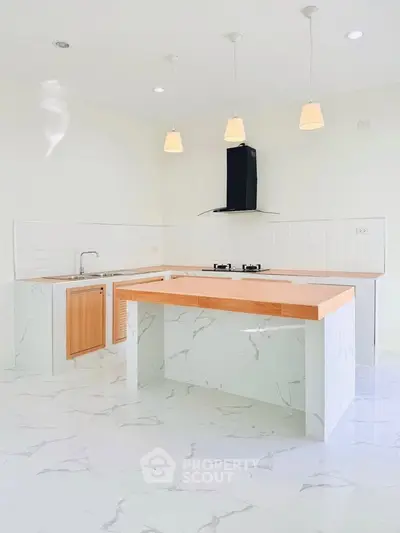 Modern kitchen with marble flooring and island, featuring sleek pendant lighting and gas stove.