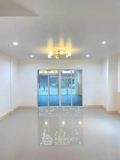 Spacious modern living room with glossy tiled floors and elegant lighting, featuring large sliding glass doors.
