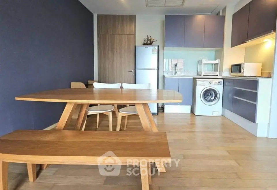 Modern kitchen with wooden dining set, washing machine, and sleek appliances in a stylish apartment.