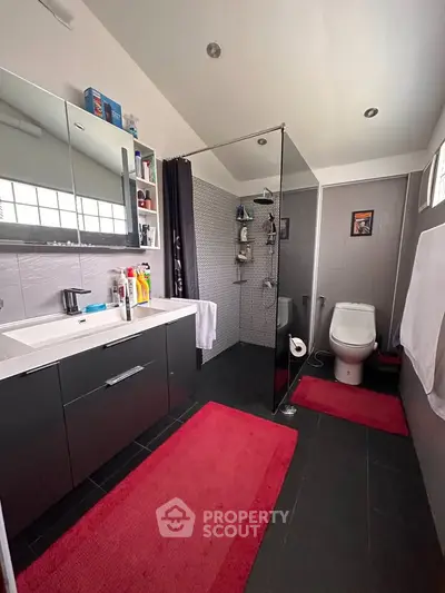 Modern bathroom with sleek fixtures and red accents, featuring a spacious shower and contemporary design.