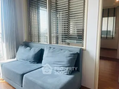 Modern living room with cozy blue sofa and large windows with blinds, offering a bright and inviting atmosphere.