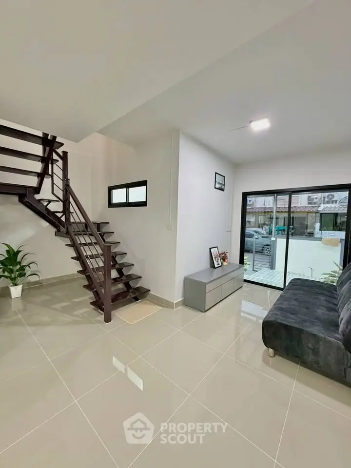 Modern living room with sleek staircase and large window, offering a bright and spacious ambiance.