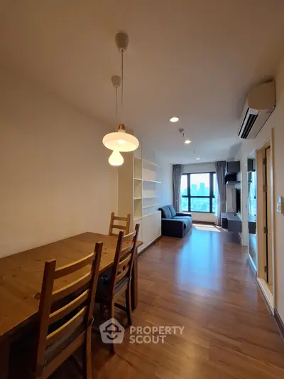 Spacious living room with wooden flooring and modern furniture, featuring a large window with city view.