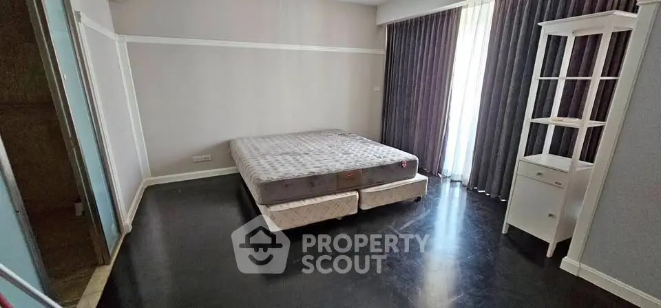 Spacious bedroom with large window and elegant dark flooring, perfect for relaxation and comfort.