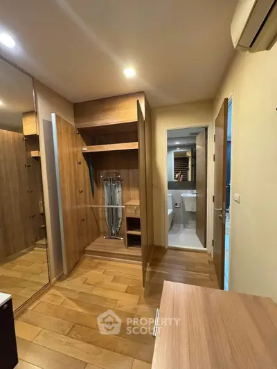 Spacious walk-in closet with wooden flooring and modern design, adjacent to a sleek bathroom.