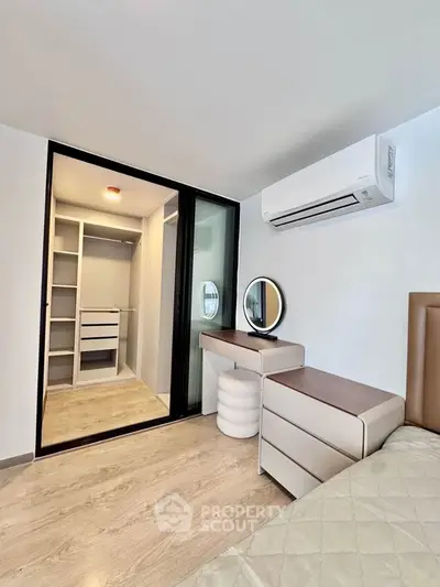Modern bedroom with walk-in closet and air conditioning, featuring sleek furniture and wooden flooring.
