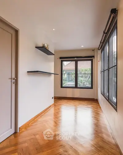 Spacious room with wooden flooring and large windows offering natural light.