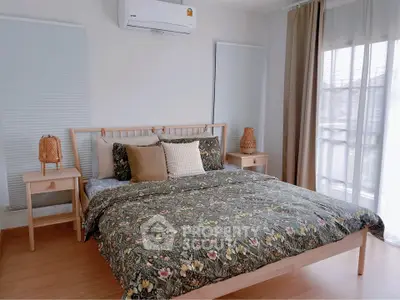 Cozy bedroom with floral bedding, wooden furniture, and natural light from large window.