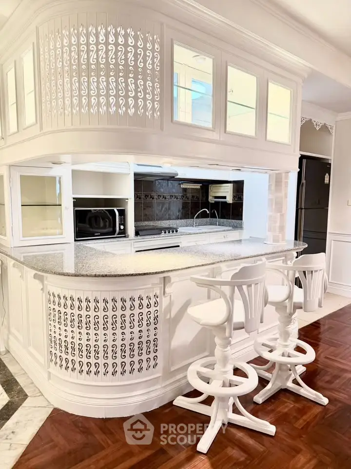 Elegant kitchen with white cabinetry and breakfast bar, featuring modern appliances and stylish bar stools.