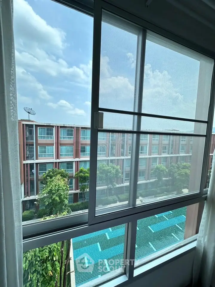 Modern apartment view with pool and lush greenery under a clear blue sky.