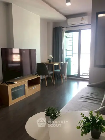 Modern living room with large TV, cozy sofa, and dining area near balcony.