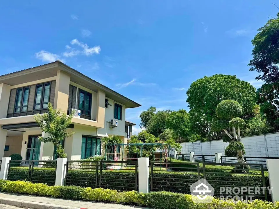 Modern two-story house with lush garden and manicured hedges under clear blue sky.