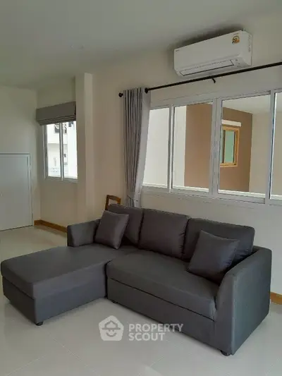 Modern living room with sleek gray sofa and large windows, featuring a minimalist design and ample natural light.