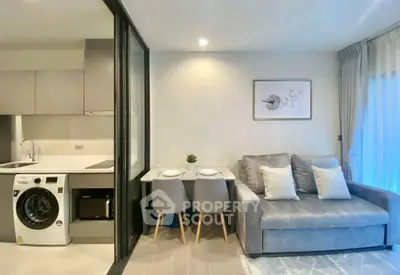 Modern living room with cozy sofa, dining area, and integrated kitchen featuring a washing machine.