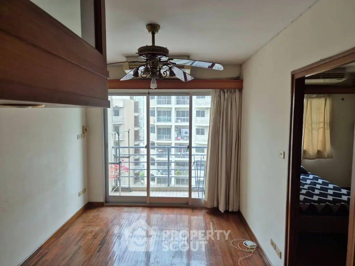 Cozy apartment with wooden flooring and ceiling fan, featuring a small balcony with city view.