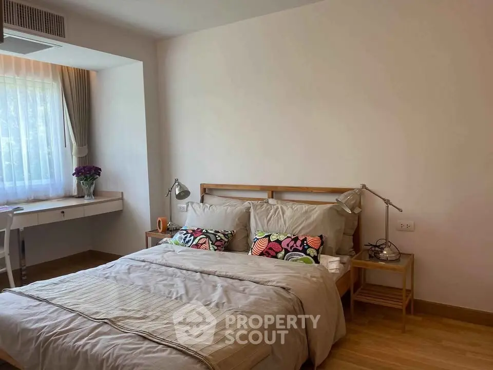 Cozy bedroom with natural light, wooden flooring, and stylish decor in a modern apartment.