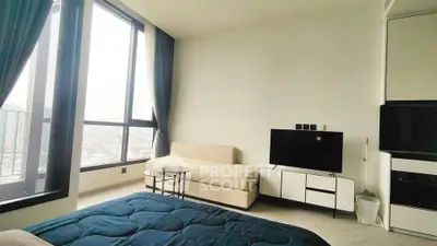 Modern bedroom with large windows and city view, featuring a cozy sofa and sleek TV setup.