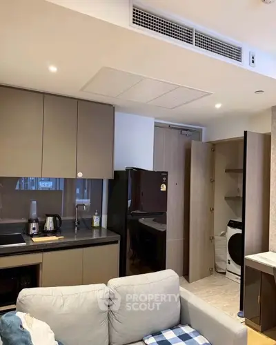 Modern kitchen with sleek cabinetry, black appliances, and cozy living area in open layout apartment.