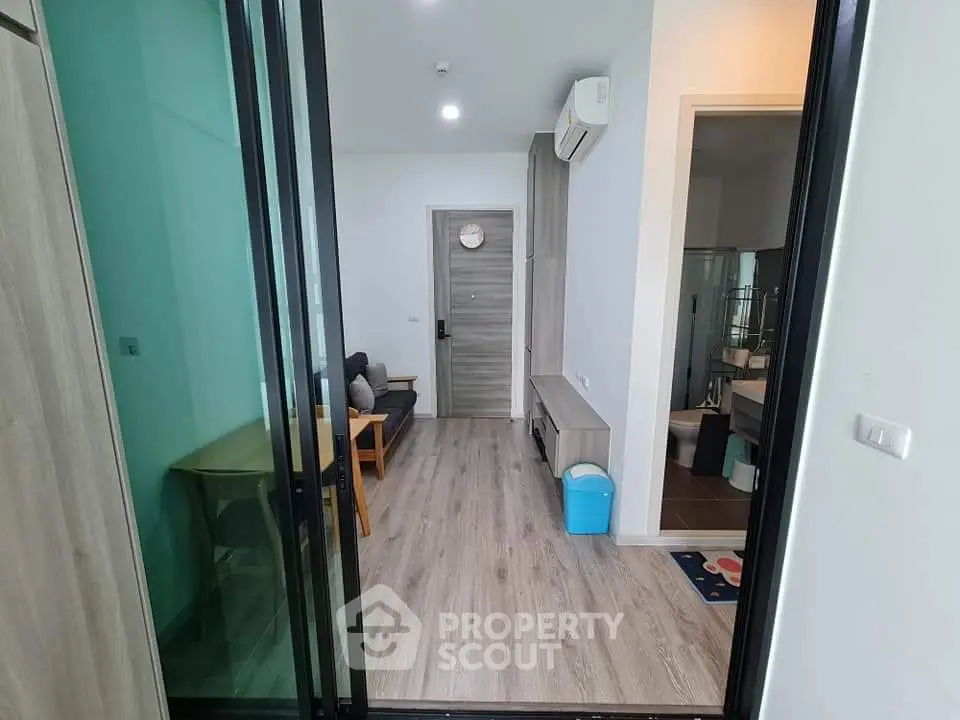 Modern apartment interior with open living space and visible bathroom, featuring sleek design and wooden flooring.