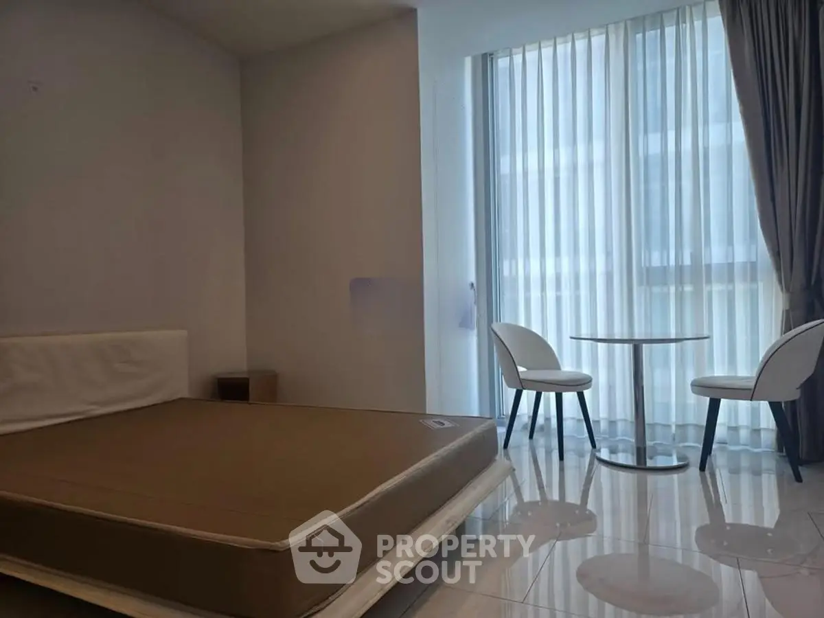 Modern minimalist bedroom with large window and elegant seating area.