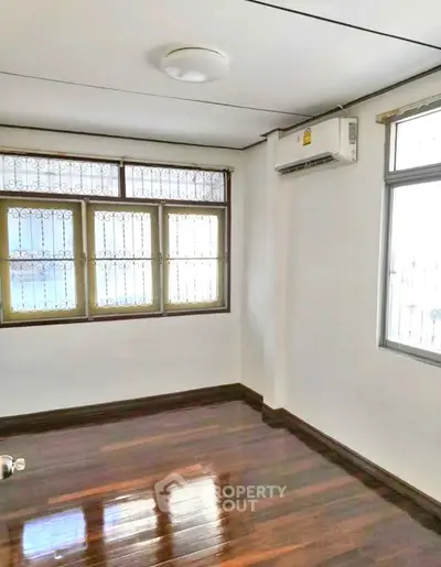 Bright empty room with polished wooden floors and large windows, perfect for customization.