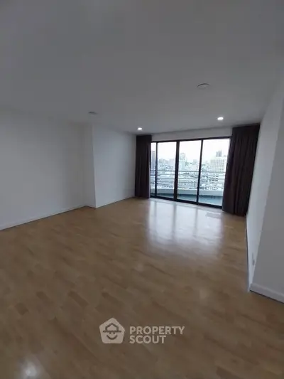 Spacious empty living room with wooden flooring and large windows offering city views.