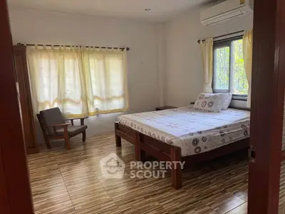 Spacious bedroom with wooden flooring and large windows for natural light.