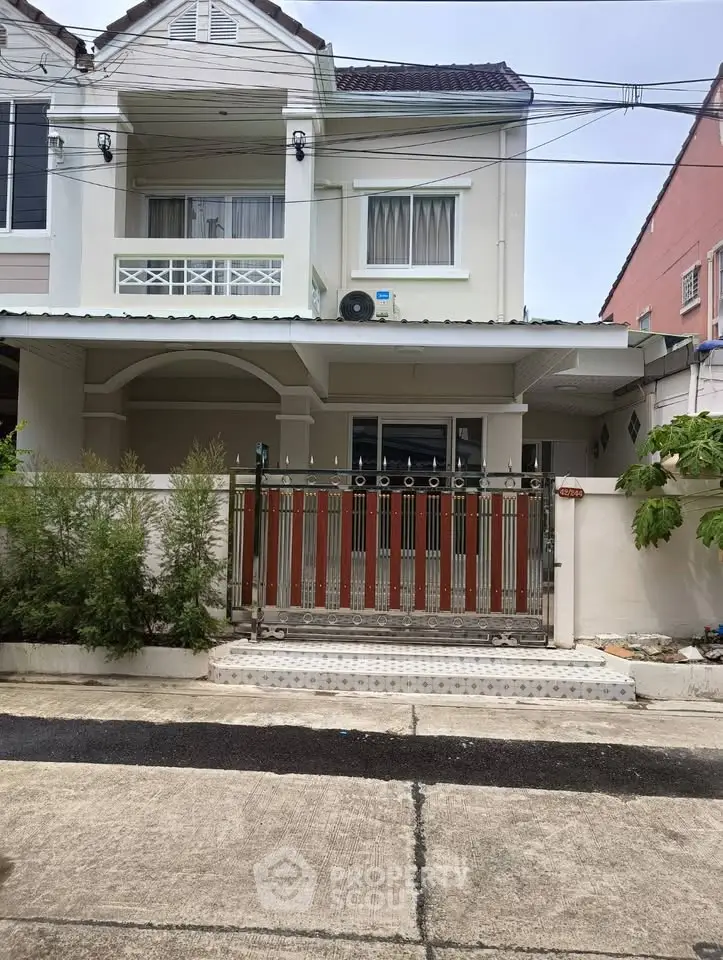 Charming two-story house with gated entrance and lush greenery in a serene neighborhood.