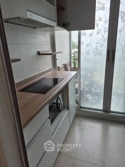 Modern kitchen with sleek induction cooktop and frosted glass sliding doors leading to a balcony.