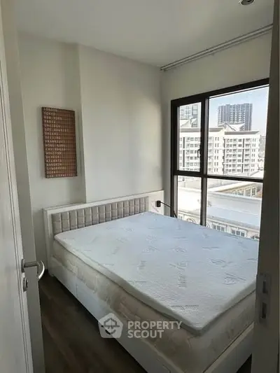 Cozy bedroom with large window offering city view, featuring a comfortable bed and modern decor.