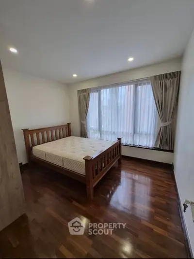 Spacious bedroom with wooden flooring and large window for natural light.