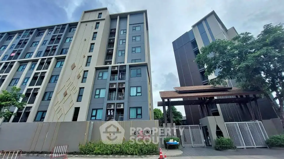 Modern apartment building exterior with gated entrance and lush greenery.