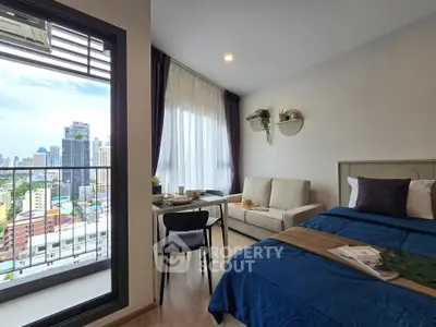 Modern studio apartment with city view, featuring cozy bed, sofa, and dining area near large window.