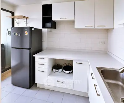 Modern kitchen with sleek white cabinets and black fridge, featuring a clean and minimalist design.