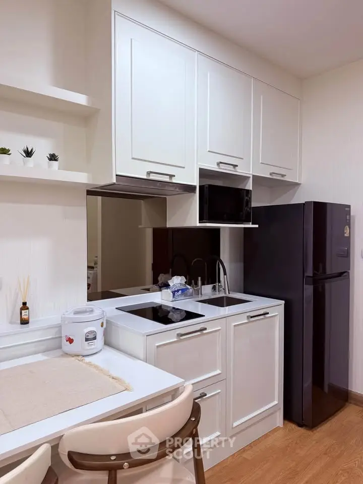 Modern kitchen with sleek white cabinets and black fridge in cozy apartment.